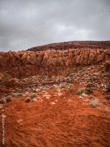 Dirt bike tracks through sandy red desert terrain below red sandstone cliffs in St. George Utah in storm photo