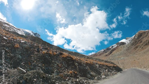 4K shot of a vehicle moving on a asphalt  road towards Zanskar Valley after crossing Shinkula Pass at Himachal Pradesh, India. Vehicle moving on a road in front of snowy Himalayas in the Zanskar. photo