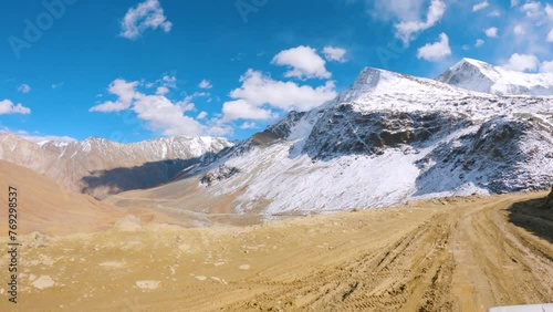 4K shot of a vehicle moving on a dirt road towards Zanskar Valley after crossing Shinkula Pass at Himachal Pradesh, India. Vehicle moving on a dirt road in front of snowy Himalayas in the Zanskar. photo