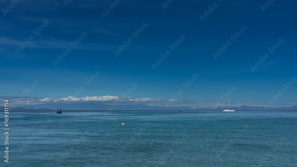 A serene seascape. Ships, boats, sailboats are visible in the boundless blue ocean. Clouds over the mountain range. Azure sky. Copy space. Madagascar.