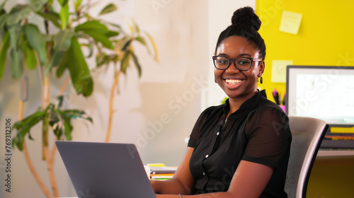 Portrait of a smiling female using a laptop in a vibrant, creative office setting. Her smile, warm and genuine, lights up the room, reflecting the satisfaction and joy of her work.