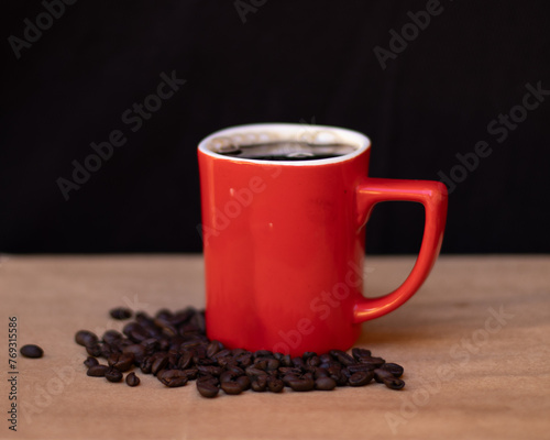 Red cup of coffee with coffee beans on wooden table. Black background.