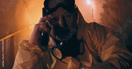 The video shows a person in a protective suit sitting in a dark nuclear bunker, holding a gun and looking at the camera, conveying alertness after a nuclear event. photo