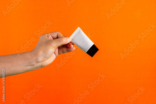 Plastic white tube for cream or lotion. Skin care or sunscreen cosmetic in hand on orange background.