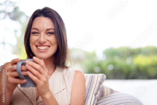 Woman, home and smile in couch with tea to relax or chill on break, day off and enjoy. Portrait, female person and happy in living room on sofa with cup of coffee for rest and calm in lounge.