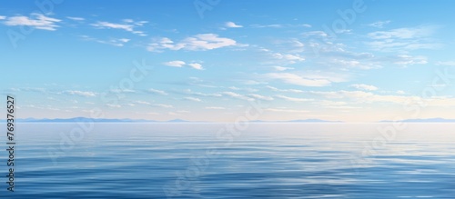 A vast expanse of liquid blue water meets the sky, with fluffy cumulus clouds floating in the electric blue background. The horizon blends seamlessly with the serene landscape