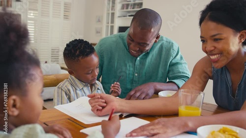 Family indoors at home sitting around table with parents helping children with homework and  grandparents in background - shot in slow motion photo