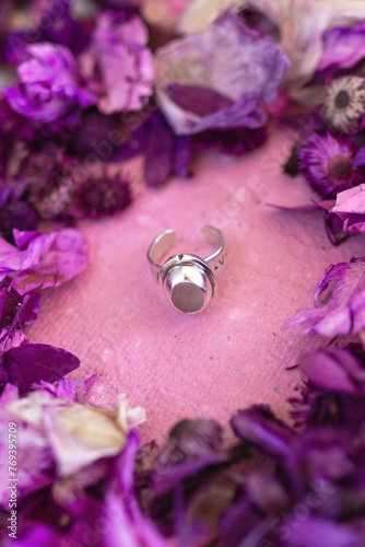 Silver ring with pink stone on a pink background with dry purple flowers. Handcraft precious item. Jewelry accessories.