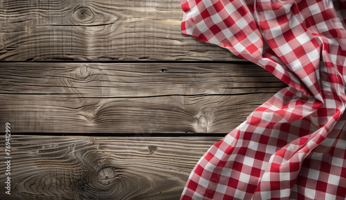 Picnic Tablecloth on Wooden Texture. The essence of a picnic is evoked with a red and white checkered tablecloth gracefully laid over a rustic, weathered wooden table, viewed from above.