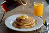 individual pouring syrup on pancakes, orange juice beside