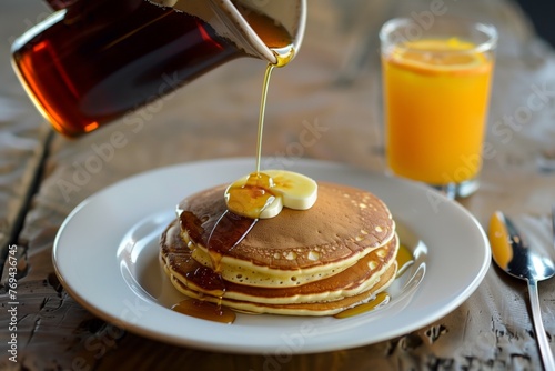 individual pouring syrup on pancakes, orange juice beside © primopiano