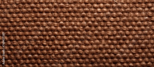 A close up of a brown rectangular fabric texture with a pattern resembling wood or wicker. The flooring material seems to be a composite material  possibly woolen or metal accents in beige tones