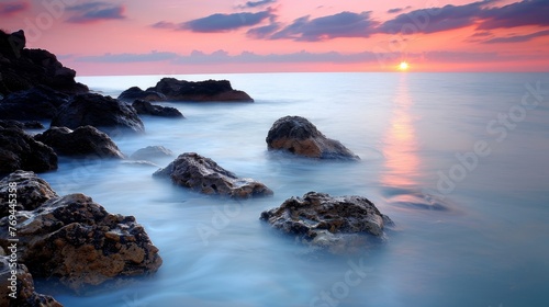 sunset over the ocean, with rocks and waves gently crashing