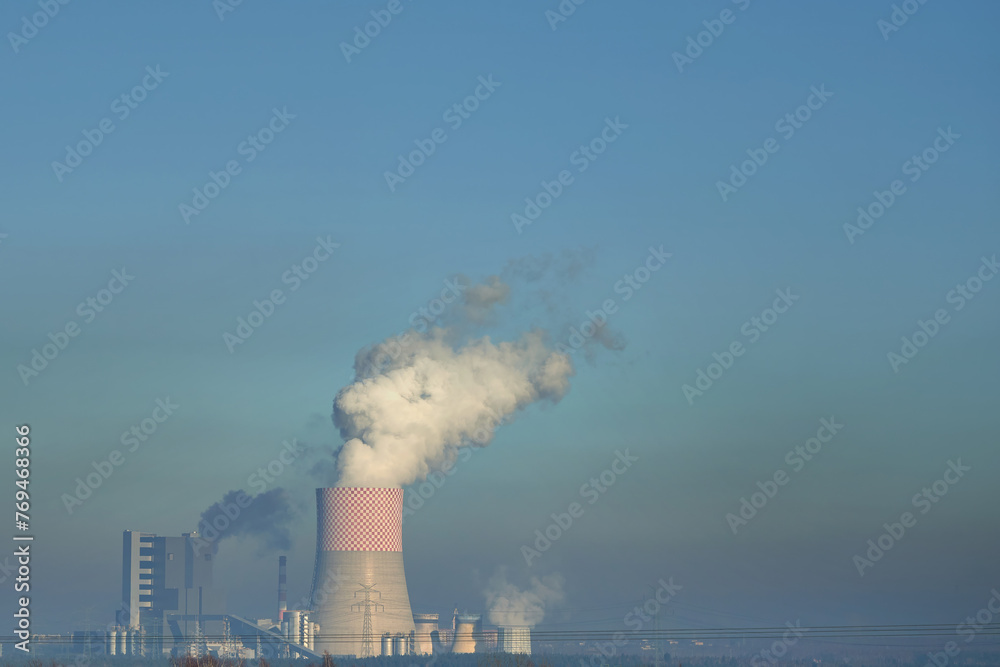 Power Plant Amidst Nature Emitting Smoke into the Clear Blue Sky. Energy generation. Cooling Towers and Chimney Stand Tall in a Field. Power Plant Amidst Nature Emitting Smoke into the Clear Blue Sky. Energy generation. Cooling Towers and Chimney Stand Tall in a Field.