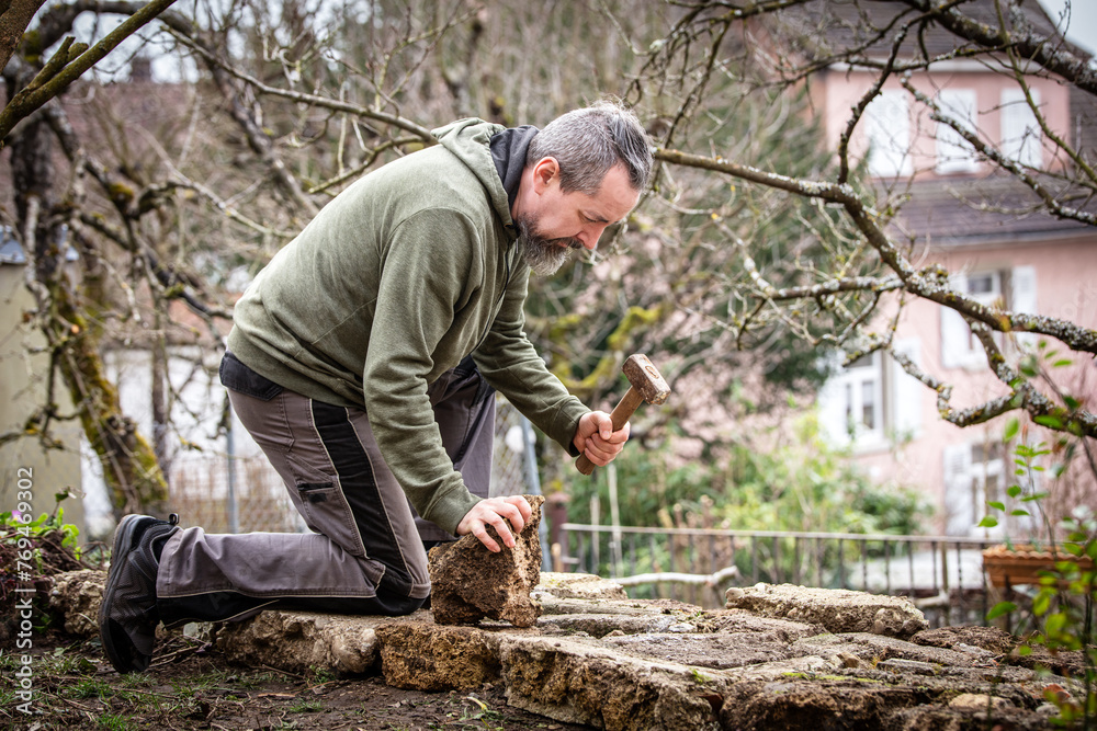 A male craftsman builds a raised bed or wall from rough stones A male craftsman builds a raised bed or wall from rough stones