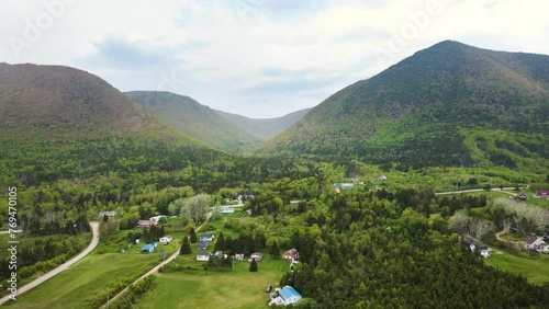 Drone shot of an incredible landscape of the Cape Breton highlands with massive mountains in the background overlooking a small village underneath located in the province of Nova Scotia in Canada. photo