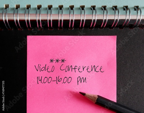 Pink note on notebook with text written Video Conference 14.00-16.00 pm, new normal work from home, remote meeting conducted in platform multiple participants can join through mobile device photo