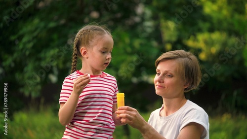 Mother and little girl find delight in shared activity of blowing soap bubbles. Park becomes place of joy as mother and daughter blow bubbles together. Mom and daughter blow bubbles slow motion