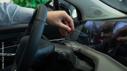 A man removes the protective film from the dashboard of a new car. 