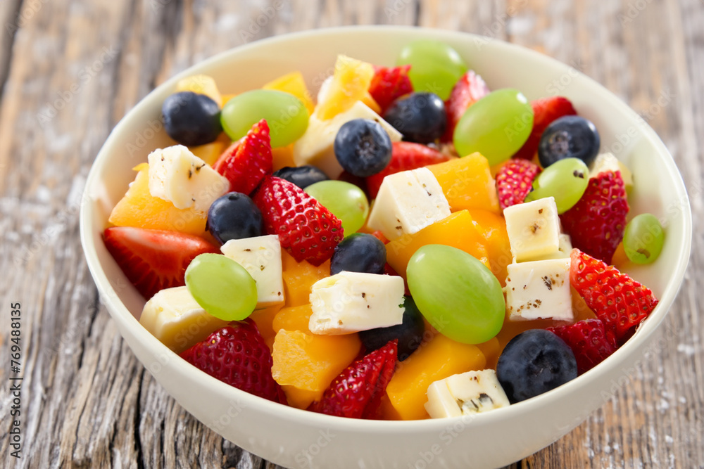 fruit salad. on a gray wooden table there is a small white plate with sliced fruits and feta cheese, top view, close up, fruit concept fruit salad. on a gray wooden table there is a small white plate with sliced fruits and feta cheese, top view, close up, fruit concept