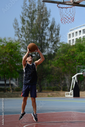 Full length of young sportsman jumping in basketball court and throwing ball to the basket © Prathankarnpap
