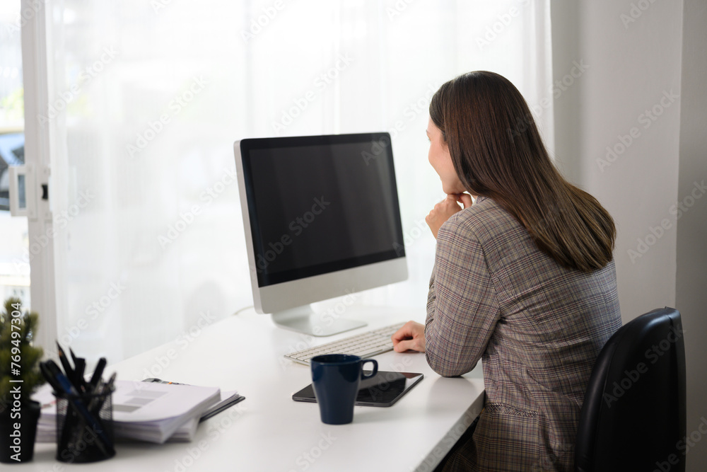 Side view of businesswoman watching online webinar on computer monitor at home office Side view of businesswoman watching online webinar on computer monitor at home office