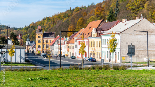 A serene view of Horni Slavkovs main street lined with colorful buildings and golden autumn foliage, under a clear blue sky. Czechia