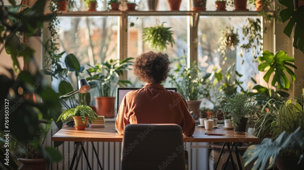 Person sits at a desk in a greenhouse surrounded by lush plants, experiencing a tranquil work environment. Person sits at a desk in a greenhouse surrounded by lush plants, experiencing a tranquil work environment.