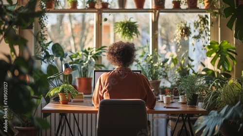 Person sits at a desk in a greenhouse surrounded by lush plants, experiencing a tranquil work environment.