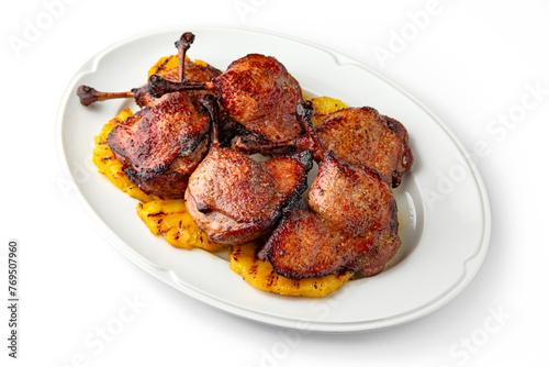 Grilled duck legs with crispy crust on a bed of grilled pineapples on a white plate. Banquet festive dishes. Gourmet restaurant menu. White background.