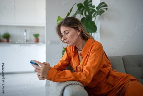 Obraz na plátně Lonely fatigued woman sitting on sofa holding smartphone sadly looking at screen scrolling web social media