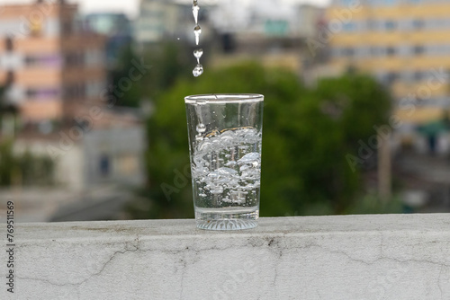 Fresh mineral drinking water is being poured into a glass causing clear bubbles to form in the glass. Water flows into a glass placed on outdoor wall. 