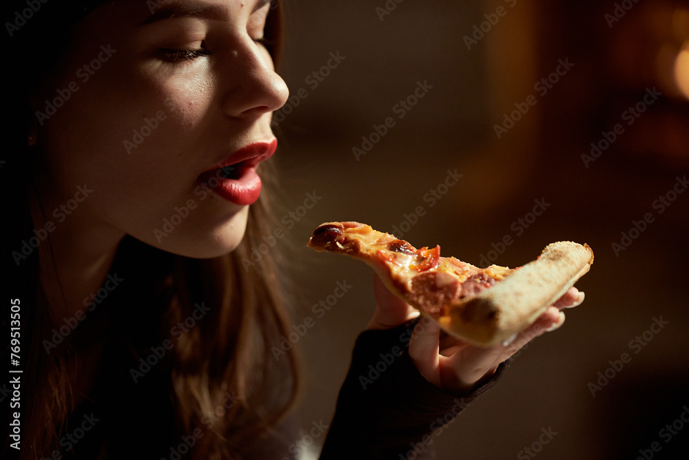 Beautiful girl with red lipstick eats pepperoni pizza in a pizzeria