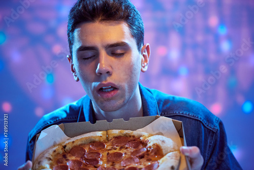 A young guy student sniffs paperoni pizza in a cardboard box