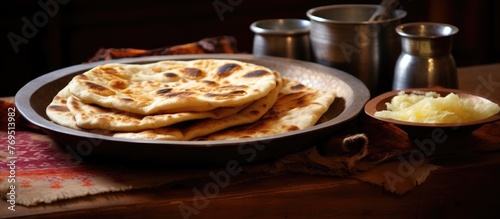 A staple food, Naan bread, is placed on a wooden table along with a bowl of butter. This traditional Indian dish is commonly served with meals like Bhakri, Chapati, and Roti