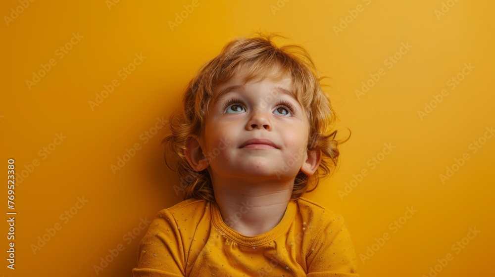 Young boy looks upwards against yellow wall. - obrazy, fototapety, plakaty 
