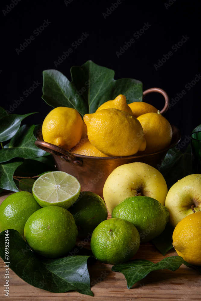Closeup of scene with lemons, limes and yellow apples with green leaves on table, black background vertically, with copy space