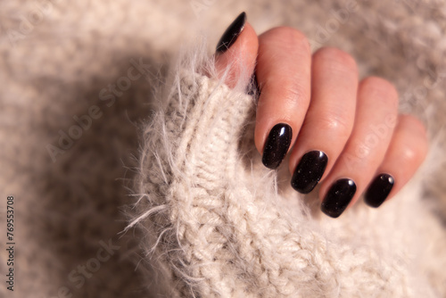 Beautiful female manicure of black color. Woman hand in cashmere knitwear photo