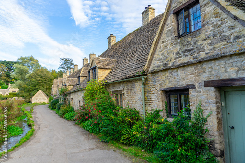Scenic view of traditional old cottage houses and a street by a river in a beautiful English village, Bibury village in the Cotswolds Area of Outstanding Natural Beauty in Cirencester, England. photo