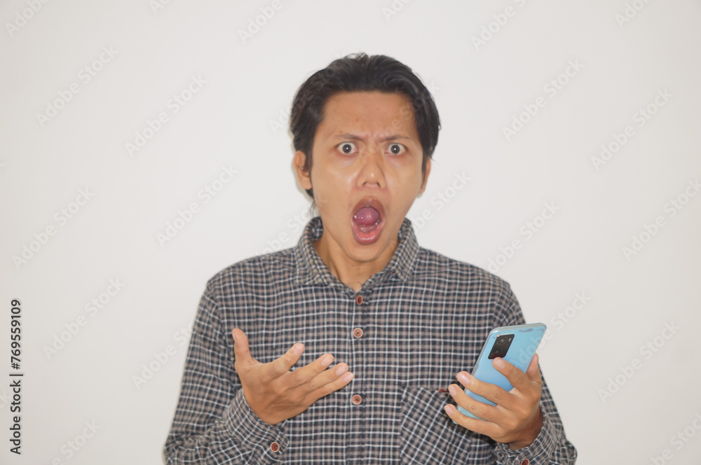 Young Asian man wearing black shirt surprised while looking at smartphone isolated on white background. - obrazy, fototapety, plakaty 