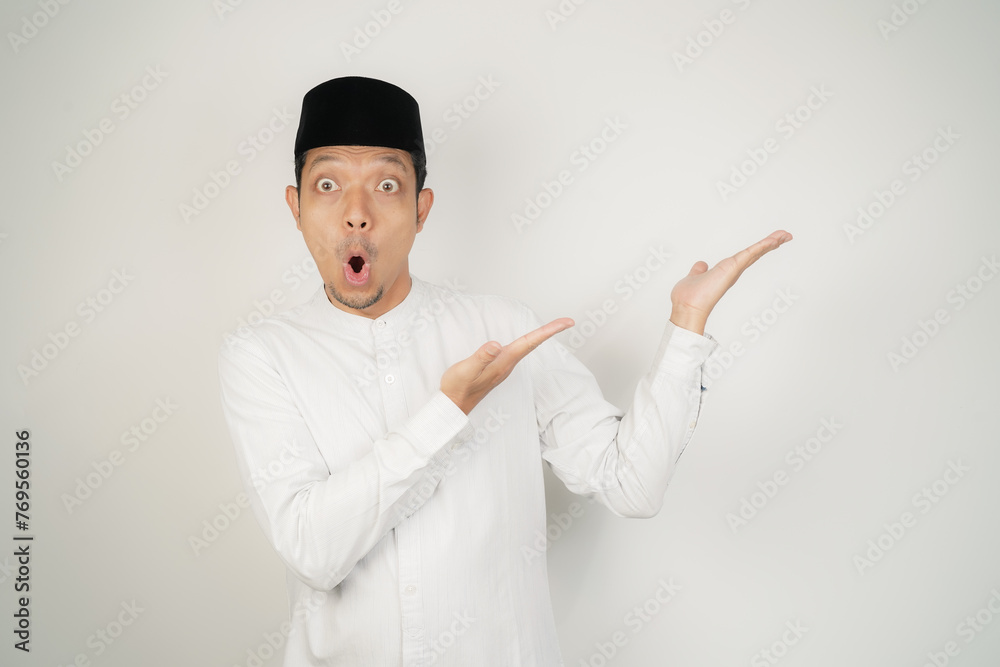 Wow face shocked expression Asian Muslim man wearing Arab costume pointing hand finger at empty space on isolated background - obrazy, fototapety, plakaty 