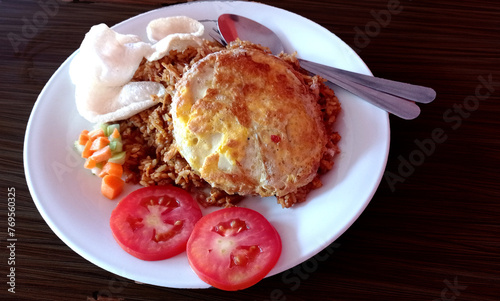 Fried rice topped with egg, crackers and pickled pieces on a white plate and wooden table