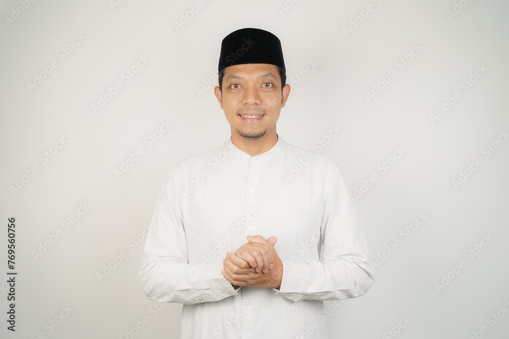 Happy smiling Asian Muslim man in Arabic costume standing with Eid greeting gesture and welcoming Ramadan isolated background - obrazy, fototapety, plakaty 