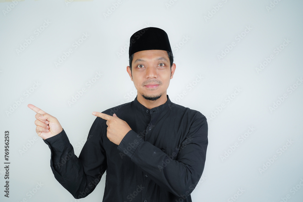 Cheerful handsome Asian Muslim man pointing hand finger at empty space for advertising on isolated background - obrazy, fototapety, plakaty 