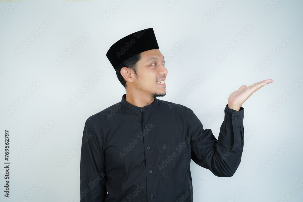 Cheerful handsome Asian Muslim man pointing hand finger at empty space for advertising on isolated background - obrazy, fototapety, plakaty 