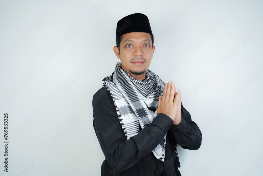 Happy smiling Asian Muslim man in Arabic turban sorban standing with Eid greeting gesture and welcoming Ramadan isolated background - obrazy, fototapety, plakaty 