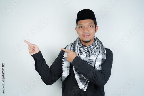Cheerful handsome Asian Muslim man wearing Arab turban sorban pointing hand finger at empty space for advertising on isolated background photo