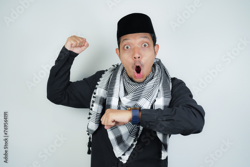 Asian Muslim man wearing Arab turban sorban Wow face shocked expression looking at watch in copy space on isolated background photo