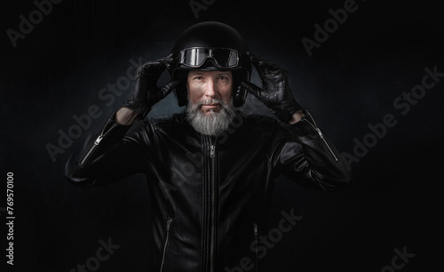 Portrait d'un motard homme avec un casque noir et une veste en cuir et des lunettes de protection et une barbe grise vintage