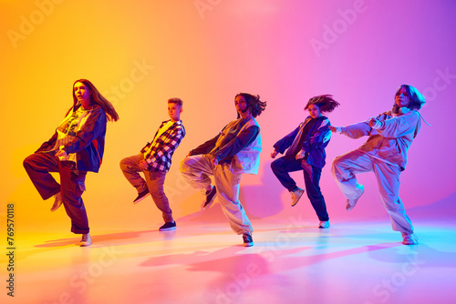 Dynamic portrait of young talented dancers dressed streetstyle clothes dancing in motion in neon light against gradient studio background. Hobby, sport, fashion, action, youth culture, music concept.